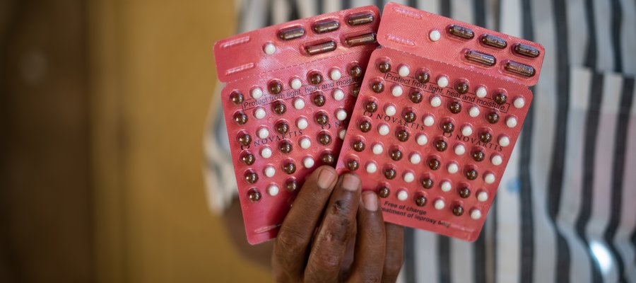 A hand holding 2 blister packs of red and white tablets